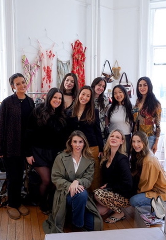 A group of VYA store owners posing together at a meetup, in front of vintage dresses and bags